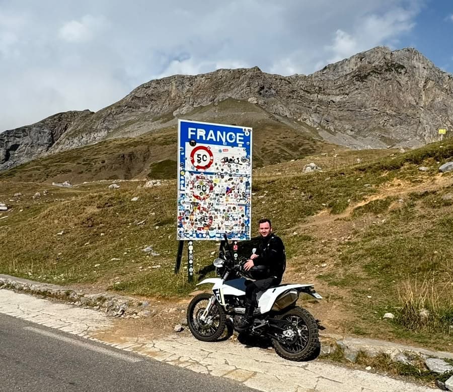 Daniel on his motorbike next to the France border sign on a mountain pass